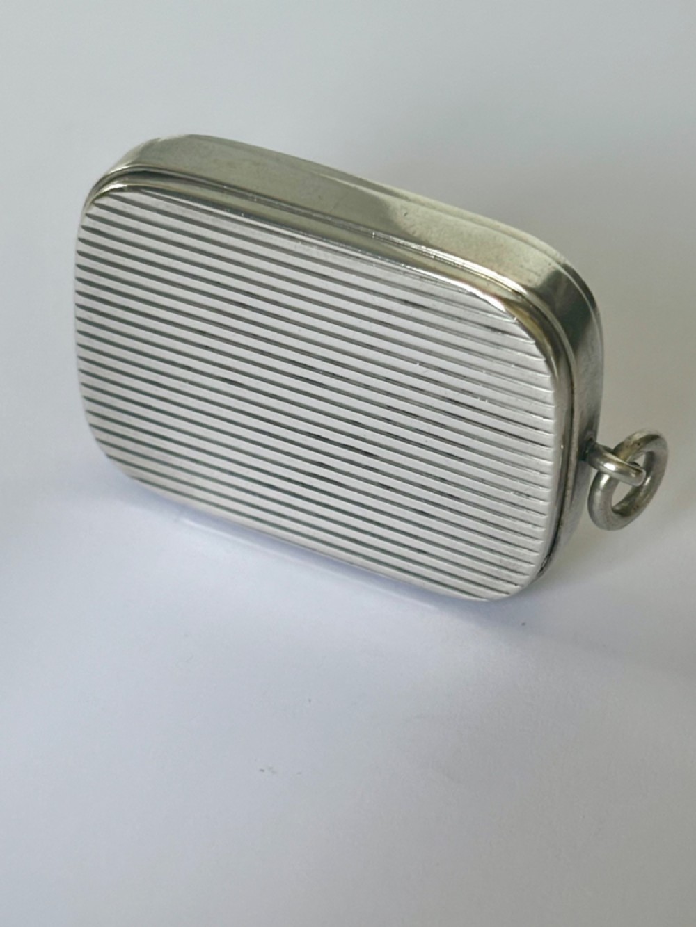 A small rectangular Victorian silver vesta case featuring horizontal reeded engine-turned decoration and an attached side suspension ring. View II