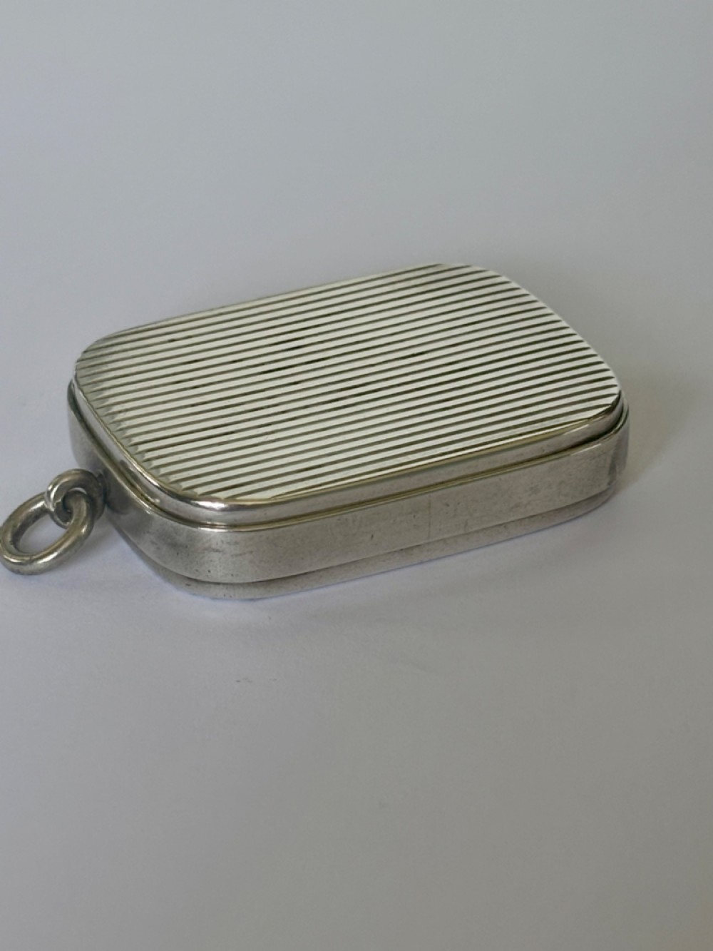 A small rectangular Victorian silver vesta case featuring horizontal reeded engine-turned decoration and an attached side suspension ring. View XII