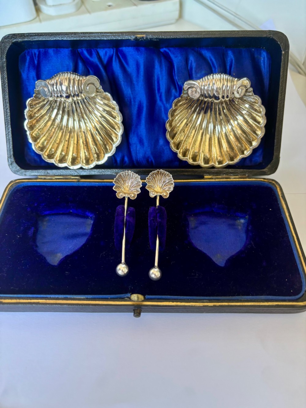 An open fitted presentation case containing two shell-shaped silver salt cellars with gilded interiors and two matching shell-bowl spoons. View II