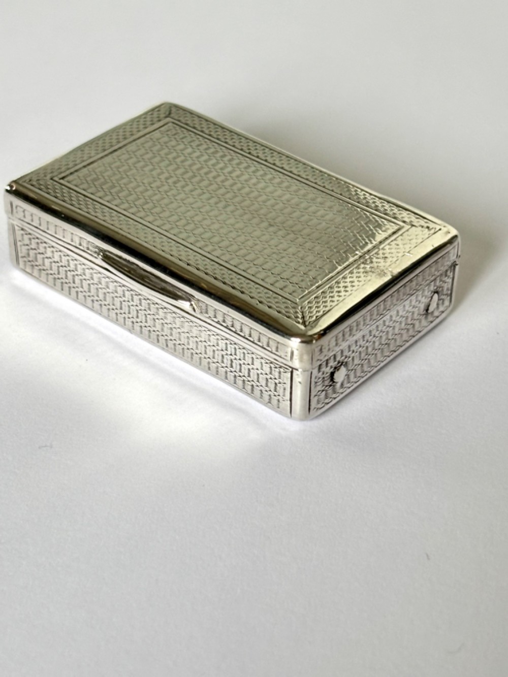 A small rectangular sterling silver snuff box with engine-turned basketweave engraving and a hinged lid.