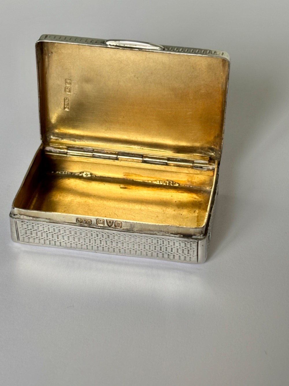 A small rectangular sterling silver snuff box with engine-turned basketweave engraving and a hinged lid. View II