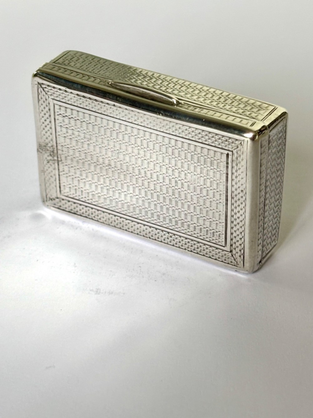 A small rectangular sterling silver snuff box with engine-turned basketweave engraving and a hinged lid. View VII