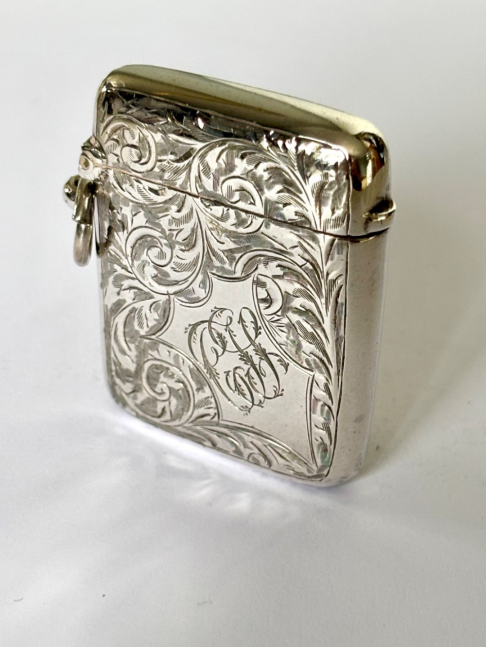 An Edwardian silver vesta case decorated with intricate foliate scroll engraving and a central monogrammed cartouche.