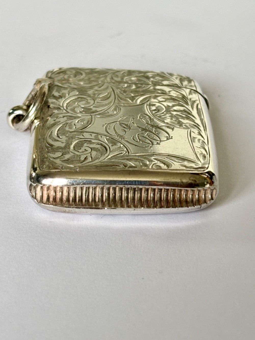An Edwardian silver vesta case decorated with intricate foliate scroll engraving and a central monogrammed cartouche. View IV