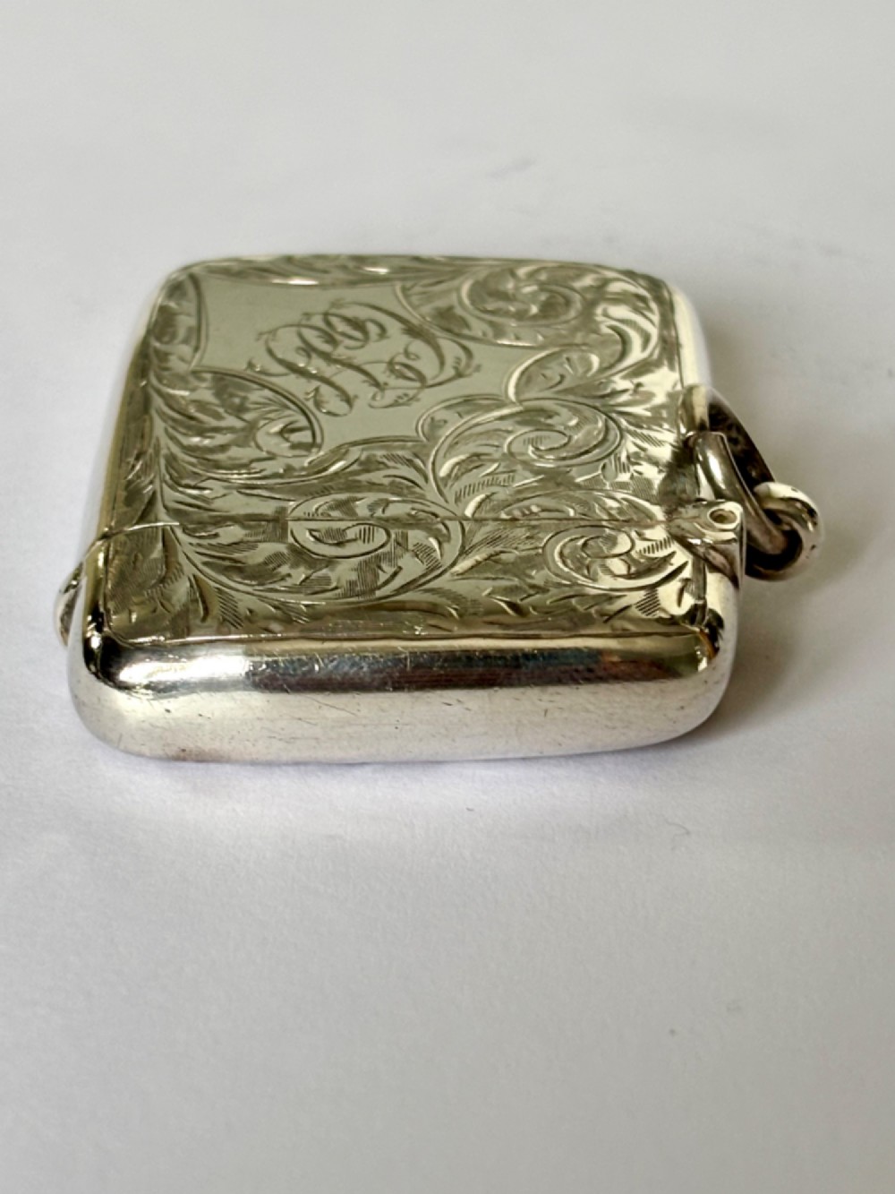 An Edwardian silver vesta case decorated with intricate foliate scroll engraving and a central monogrammed cartouche. View V