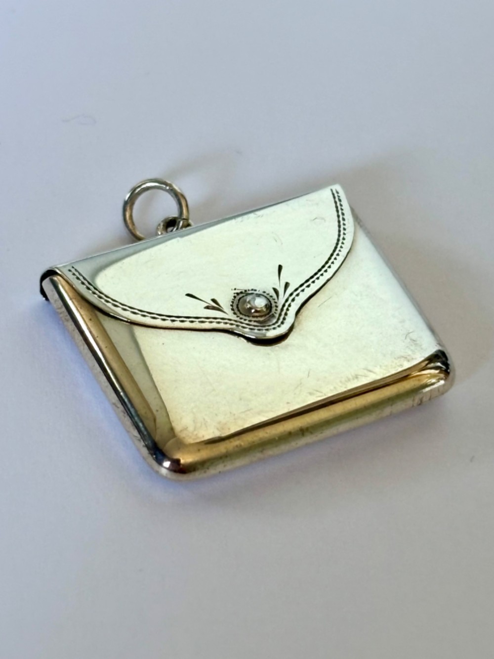 An antique sterling silver envelope-shaped stamp case featuring an engraved border and a suspension ring.