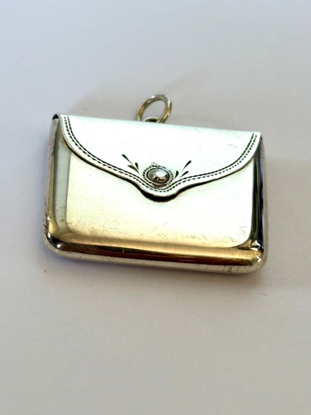 An antique sterling silver envelope-shaped stamp case featuring an engraved border and a suspension ring. View II