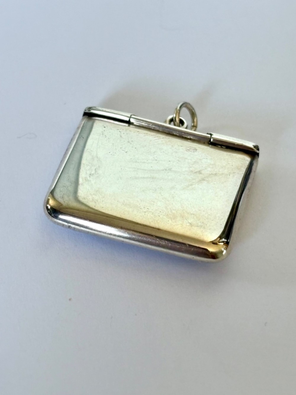 An antique sterling silver envelope-shaped stamp case featuring an engraved border and a suspension ring. View III