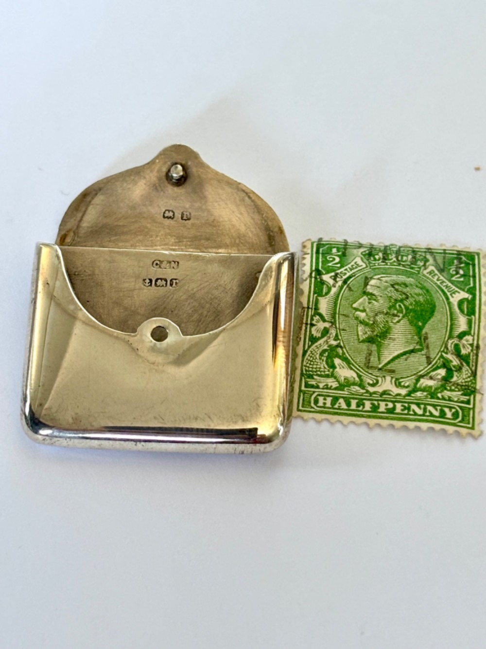 An antique sterling silver envelope-shaped stamp case featuring an engraved border and a suspension ring. View VI
