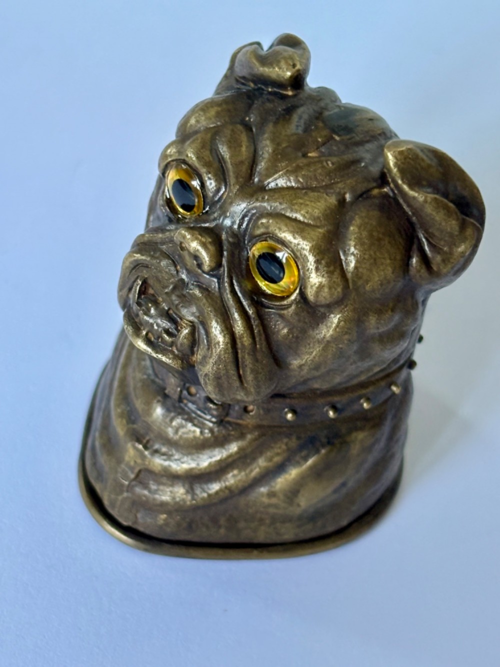 A cast brass table-top vesta case sculpted in the form of a bulldog head featuring inset yellow glass eyes and a studded collar. View X