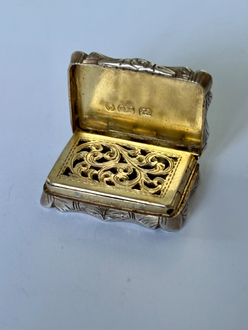 An open early Victorian rectangular silver-gilt vinaigrette showing hallmarks inside the lid and a detailed pierced foliate interior grille.