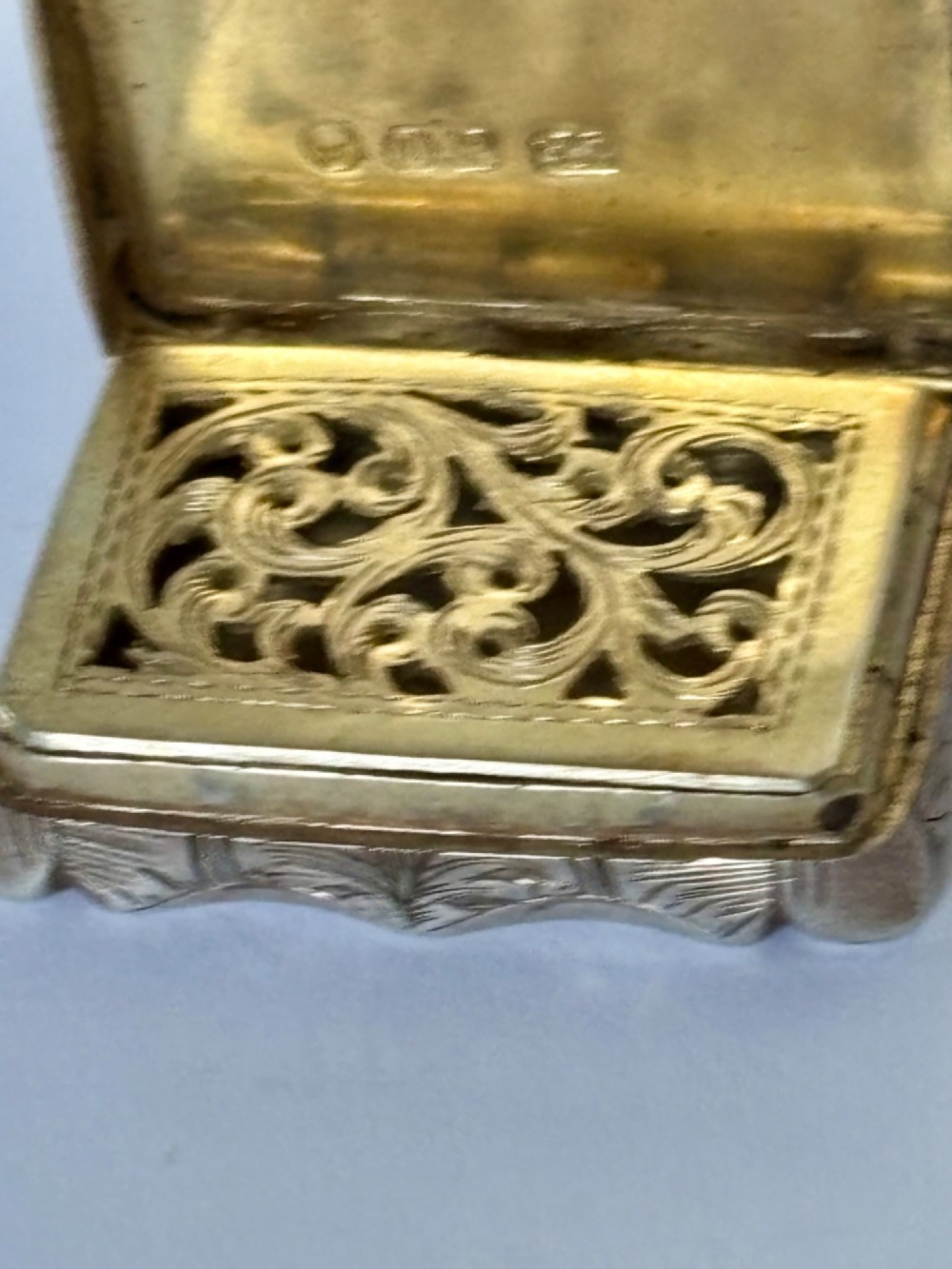 An open early Victorian rectangular silver-gilt vinaigrette showing hallmarks inside the lid and a detailed pierced foliate interior grille. View X