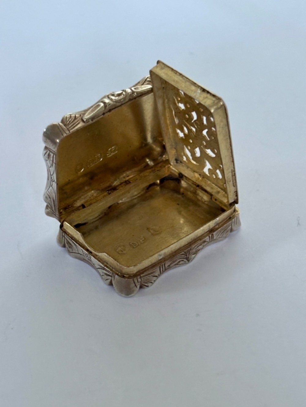 An open early Victorian rectangular silver-gilt vinaigrette showing hallmarks inside the lid and a detailed pierced foliate interior grille. View XI