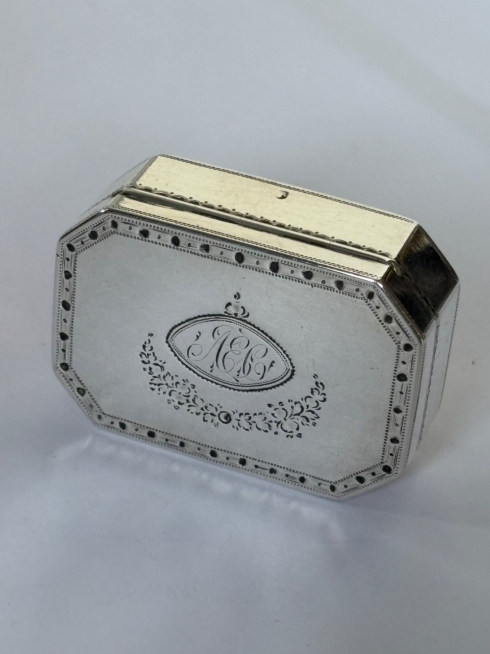 An octagonal Georgian sterling silver snuff box featuring bright-cut foliate engraving and an engraved central oval monogram.