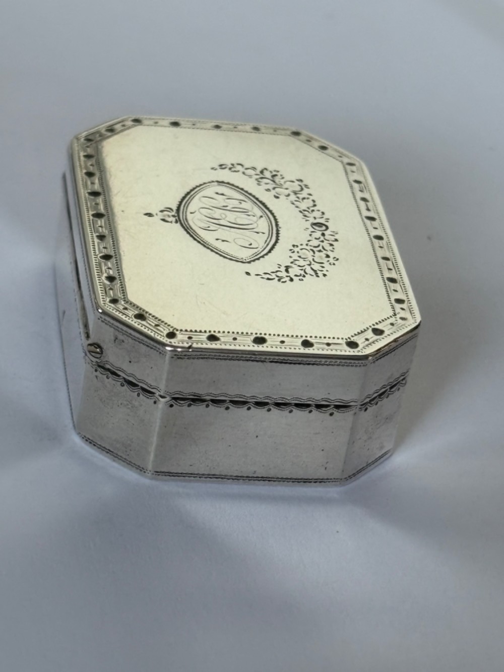 An octagonal Georgian sterling silver snuff box featuring bright-cut foliate engraving and an engraved central oval monogram. View V