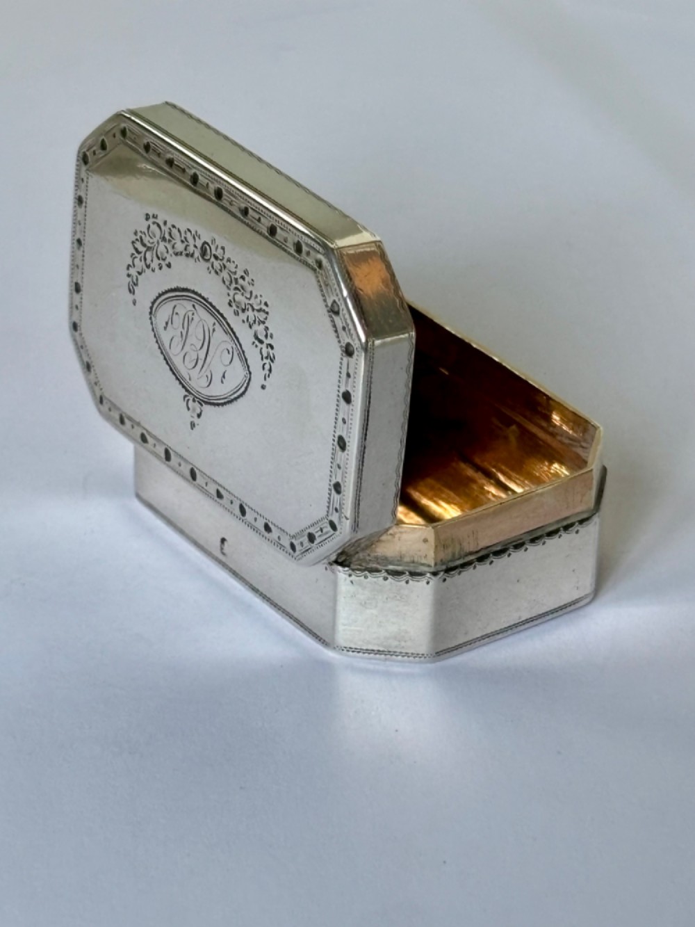 An octagonal Georgian sterling silver snuff box featuring bright-cut foliate engraving and an engraved central oval monogram. View XI