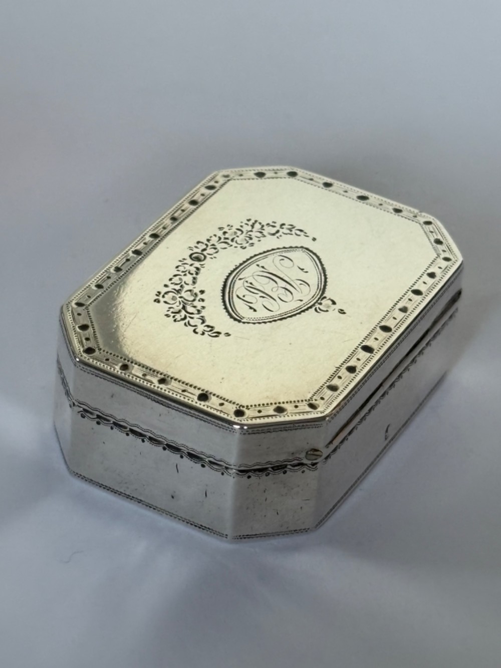 An octagonal Georgian sterling silver snuff box featuring bright-cut foliate engraving and an engraved central oval monogram. View XV