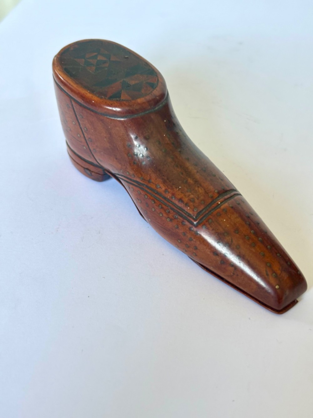 A 19th-century carved wooden shoe-form snuff box featuring brass pique pinwork and a geometric parquetry inlaid lid.