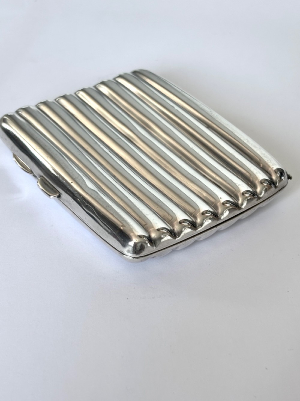 A curved sterling silver cigarette case featuring vertical fluted reeding and a push-button release mechanism.