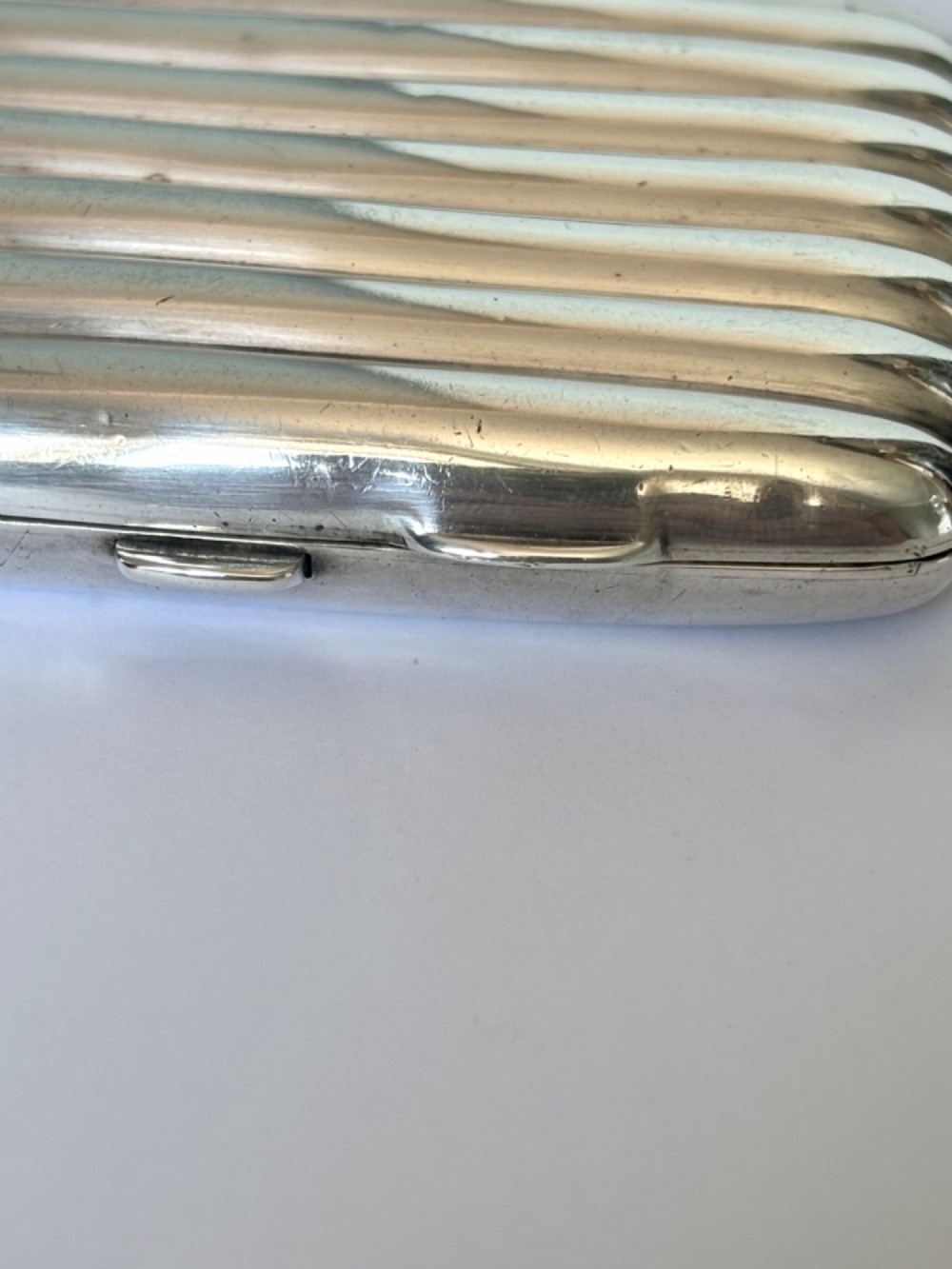 A curved sterling silver cigarette case featuring vertical fluted reeding and a push-button release mechanism. View III