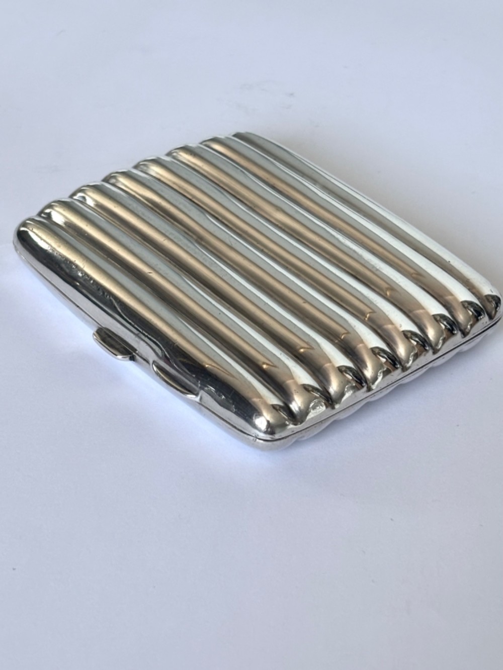 A curved sterling silver cigarette case featuring vertical fluted reeding and a push-button release mechanism. View IV