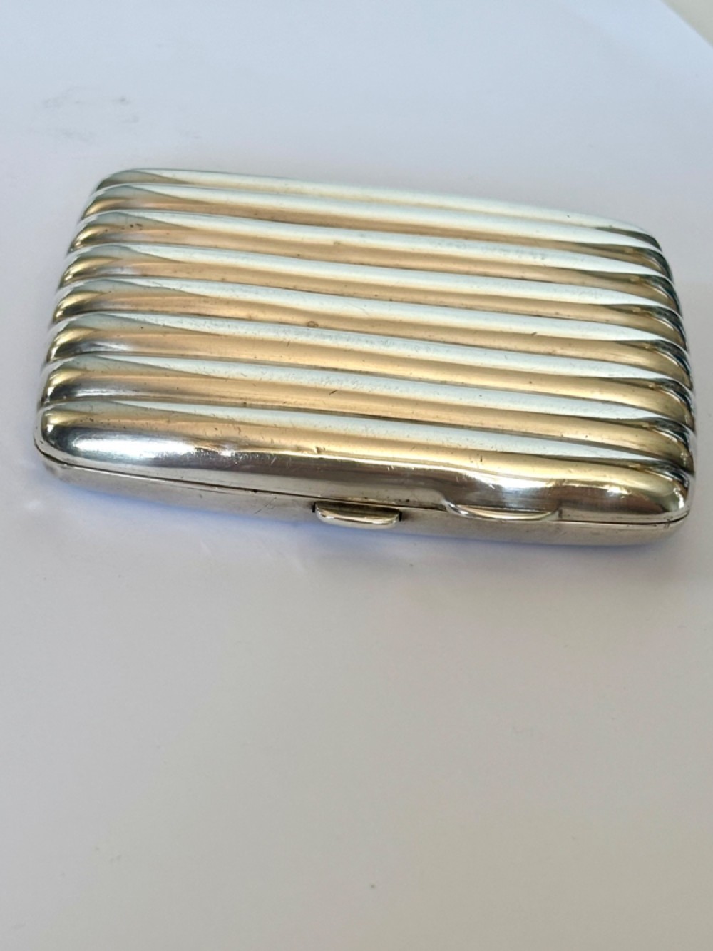 A curved sterling silver cigarette case featuring vertical fluted reeding and a push-button release mechanism. View V