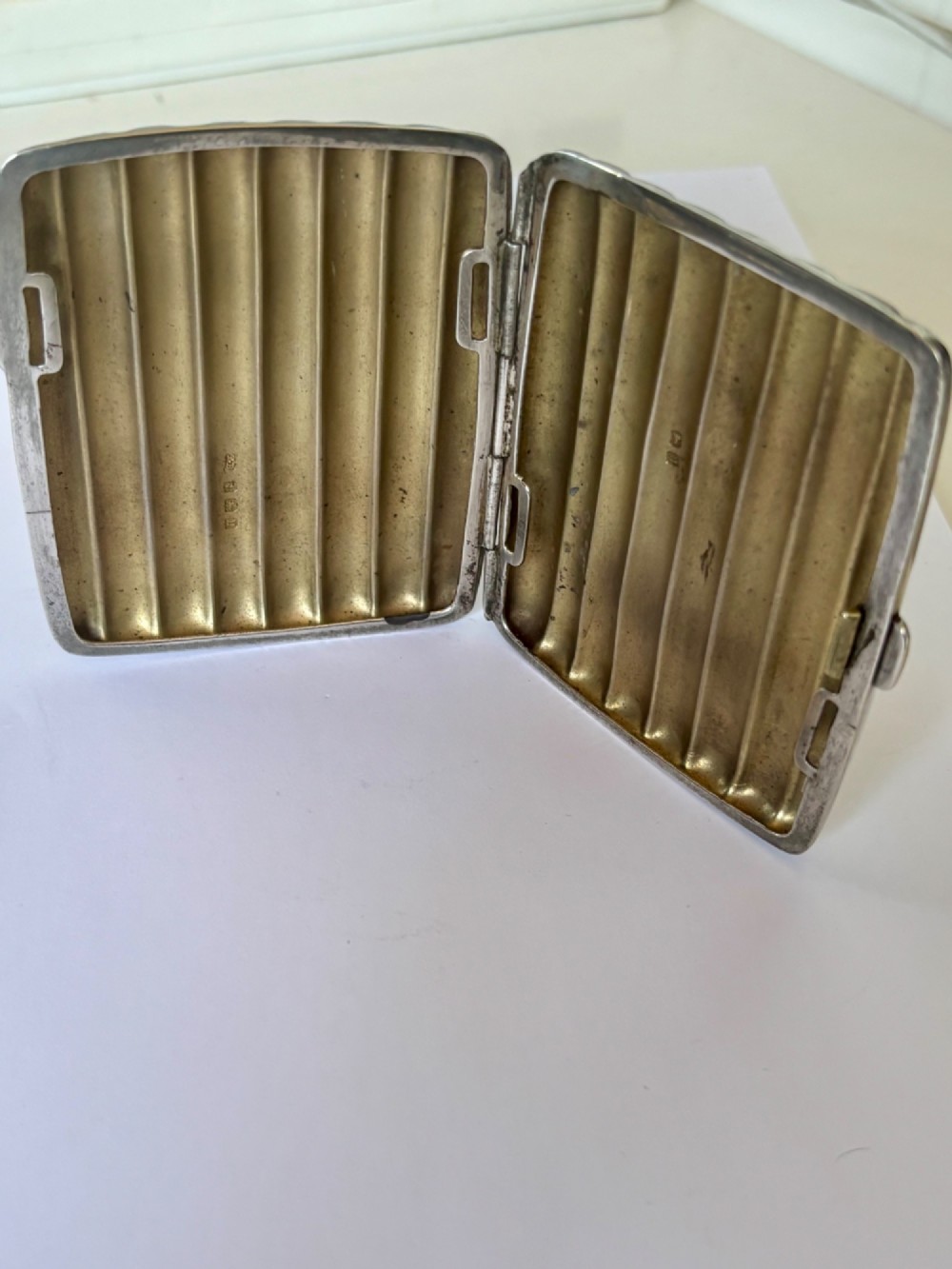 A curved sterling silver cigarette case featuring vertical fluted reeding and a push-button release mechanism. View IX