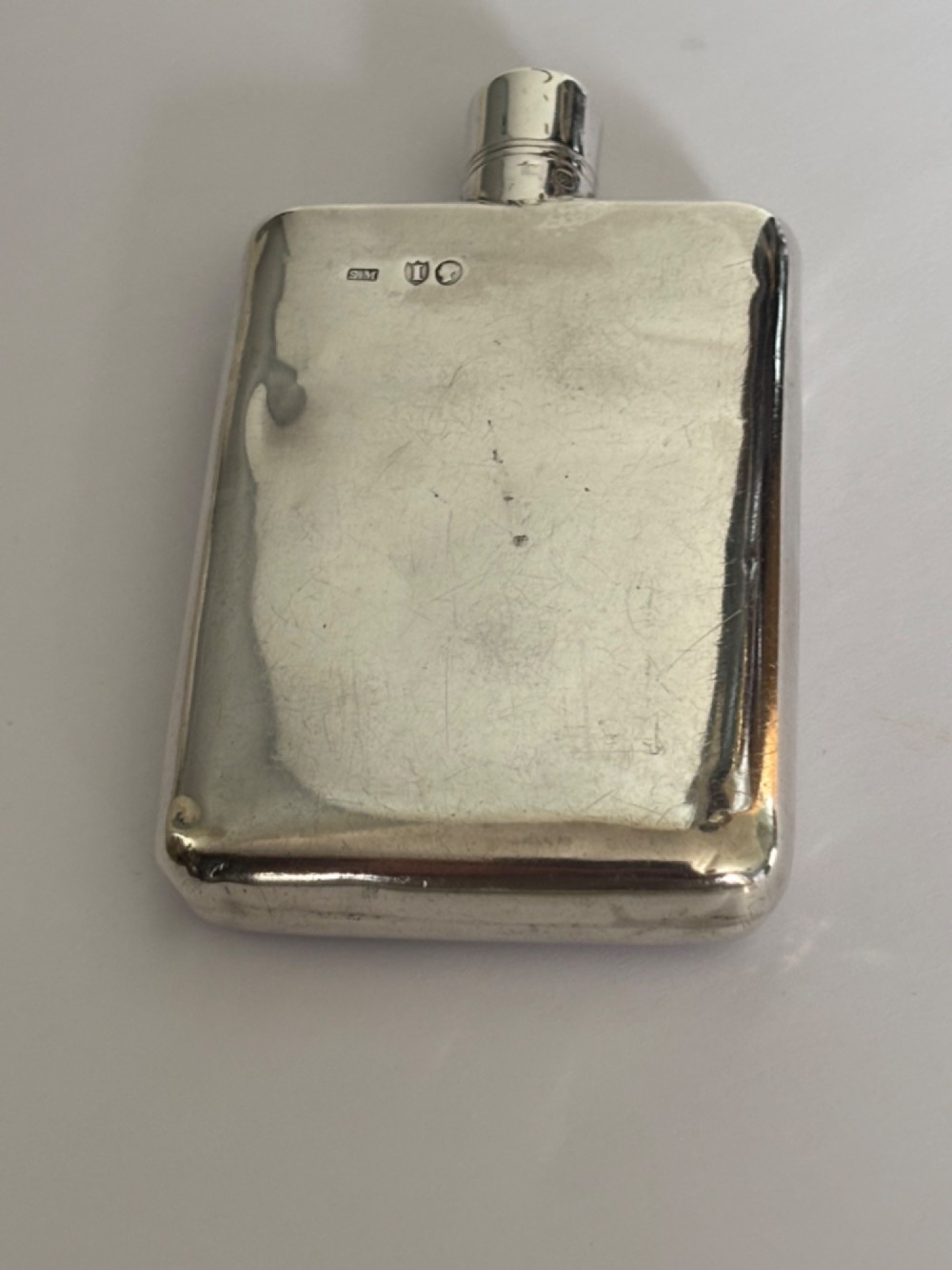 A Victorian sterling silver hip flask featuring an engraved crest, family monogram, and official British silver hallmarks. View VI