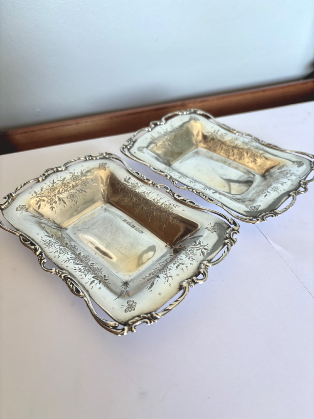 A pair of rectangular Edwardian sterling silver trinket dishes featuring pierced scrollwork borders and engraved floral decoration.