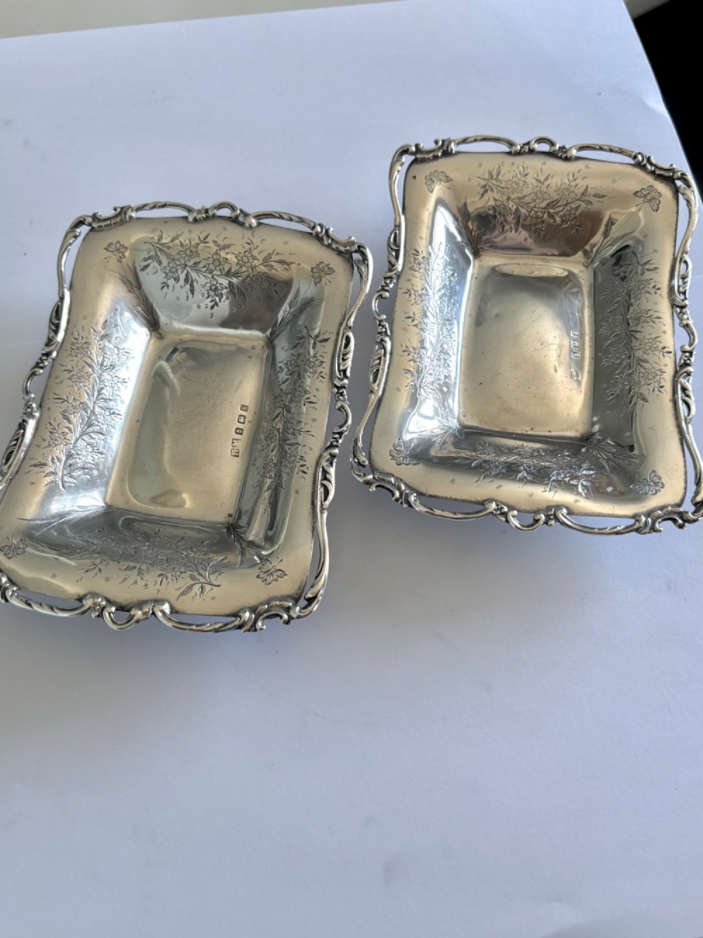 A pair of rectangular Edwardian sterling silver trinket dishes featuring pierced scrollwork borders and engraved floral decoration. View II