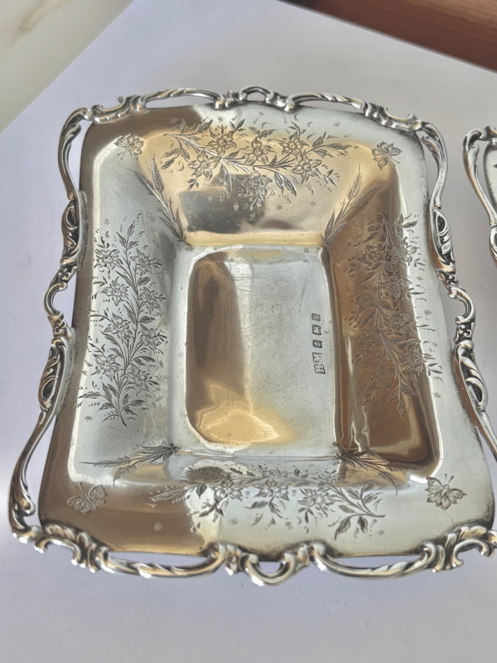 A pair of rectangular Edwardian sterling silver trinket dishes featuring pierced scrollwork borders and engraved floral decoration. View X