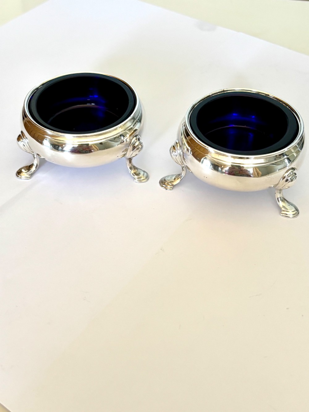 A pair of round 18th-century sterling silver open salt cellars with cobalt blue glass liners, raised on three hoof feet.