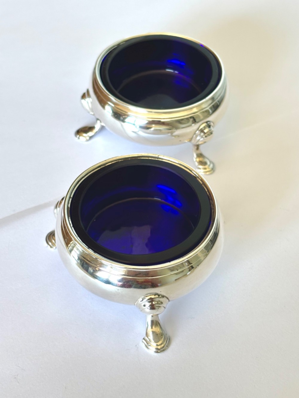 A pair of round 18th-century sterling silver open salt cellars with cobalt blue glass liners, raised on three hoof feet. View II