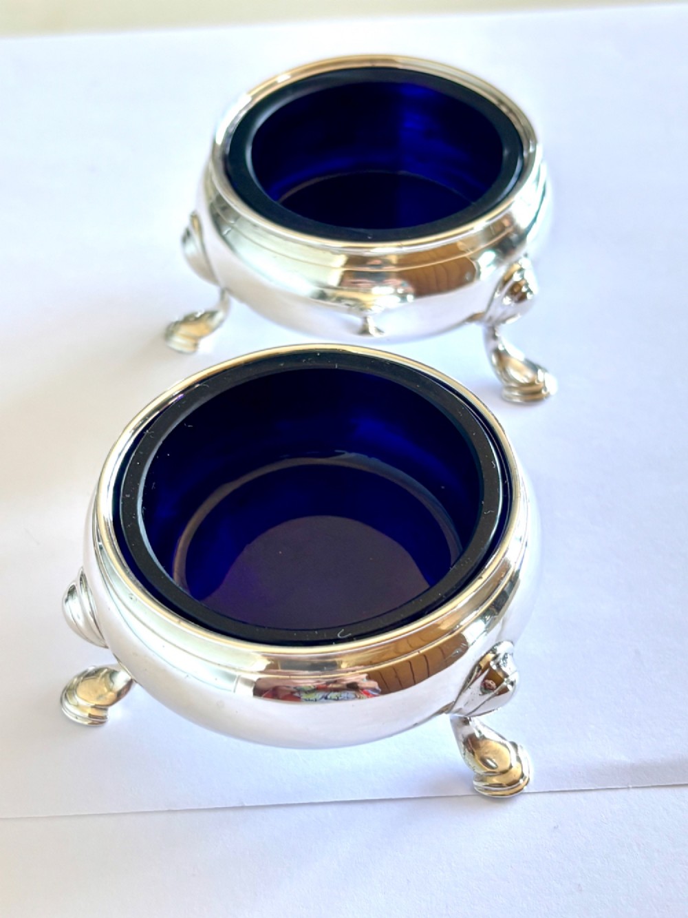 A pair of round 18th-century sterling silver open salt cellars with cobalt blue glass liners, raised on three hoof feet. View IV