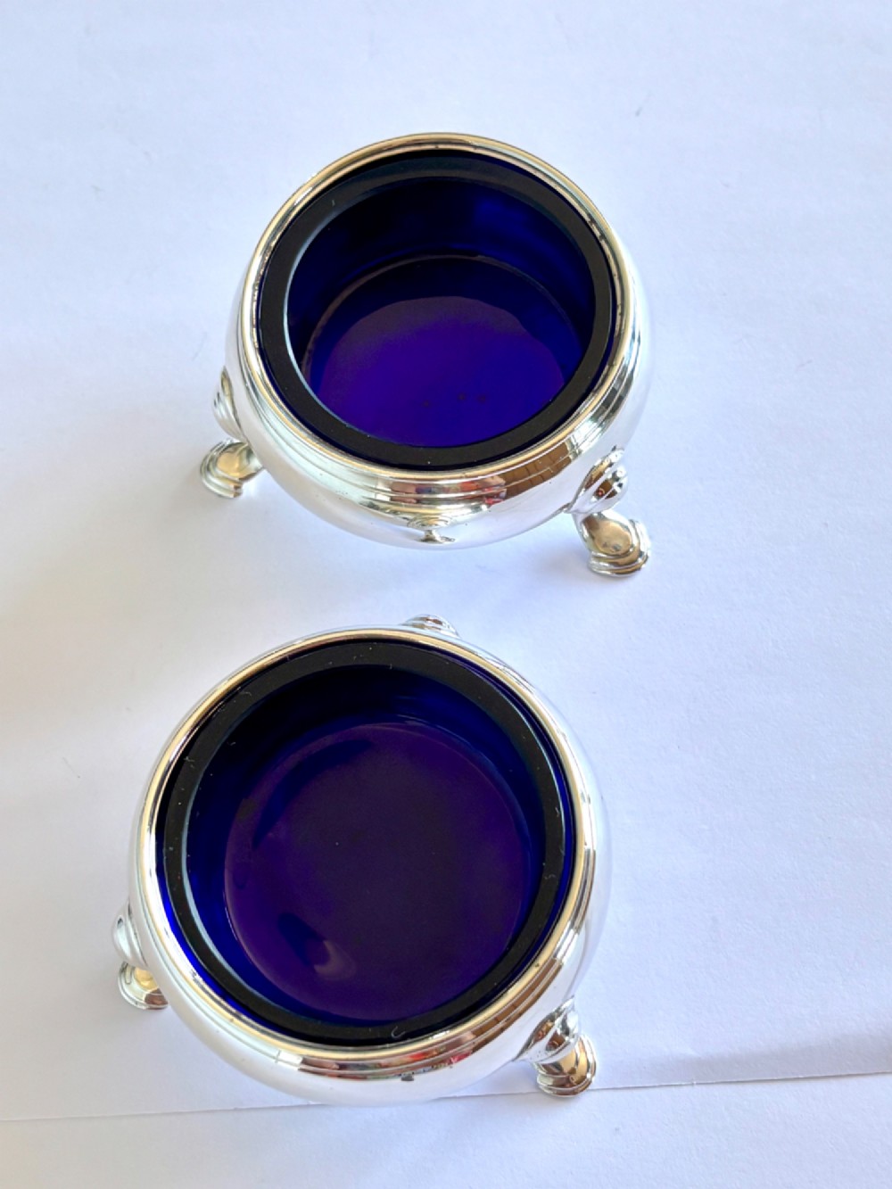 A pair of round 18th-century sterling silver open salt cellars with cobalt blue glass liners, raised on three hoof feet. View V