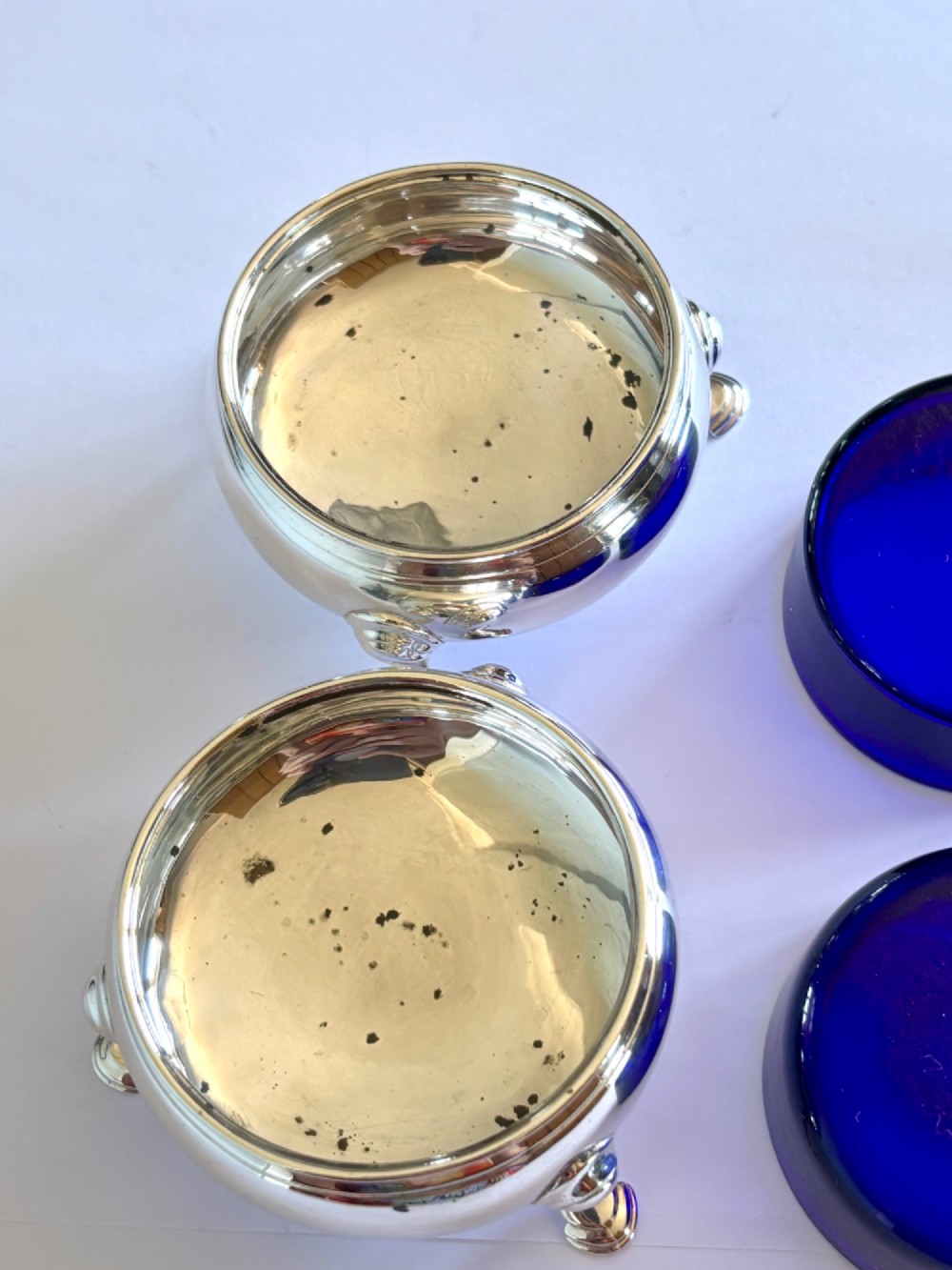 A pair of round 18th-century sterling silver open salt cellars with cobalt blue glass liners, raised on three hoof feet. View VI