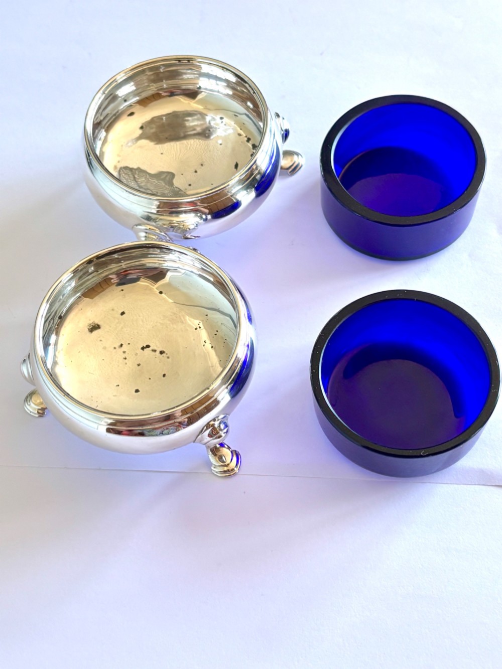 A pair of round 18th-century sterling silver open salt cellars with cobalt blue glass liners, raised on three hoof feet. View VIII