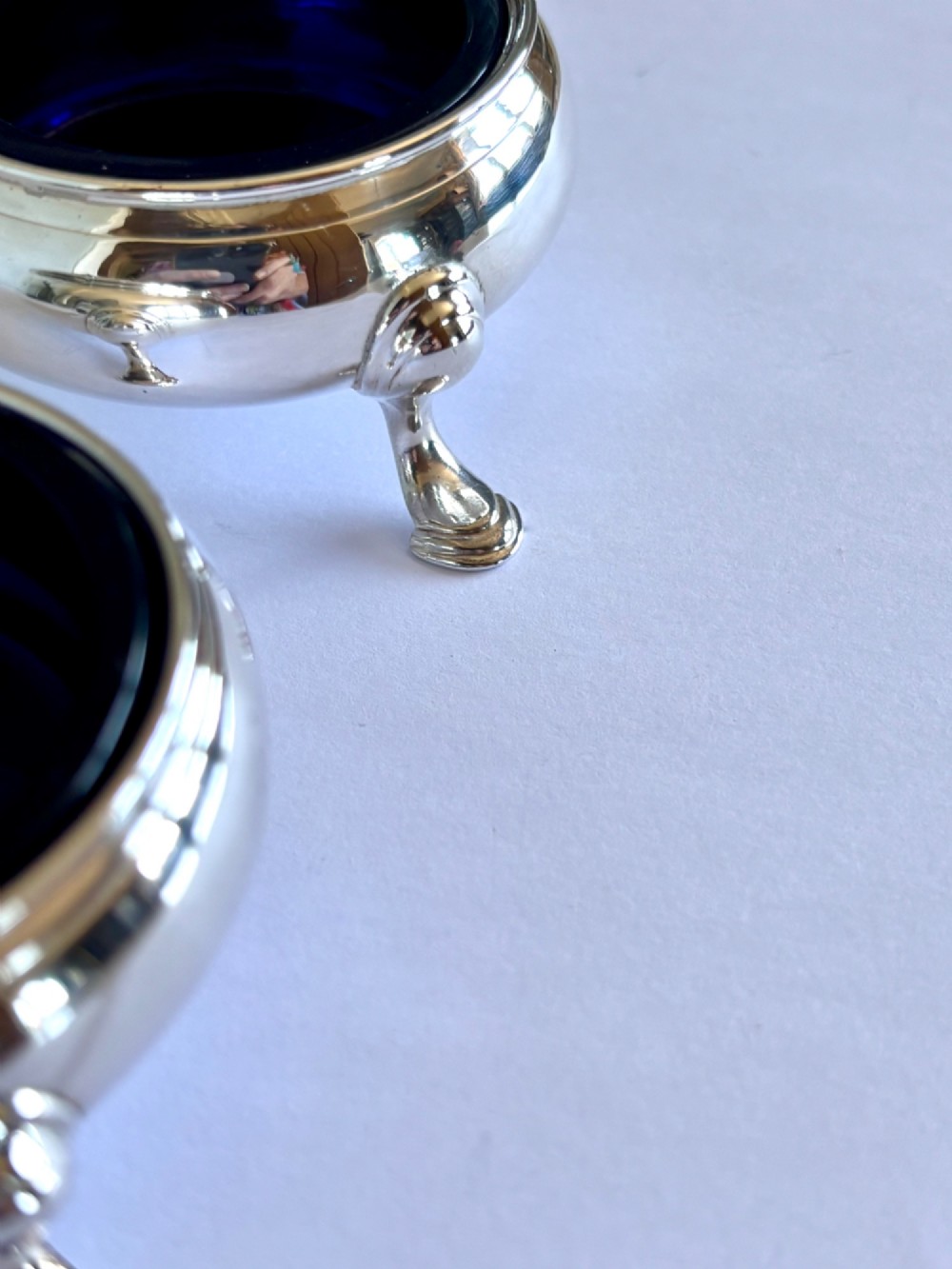A pair of round 18th-century sterling silver open salt cellars with cobalt blue glass liners, raised on three hoof feet. View IX