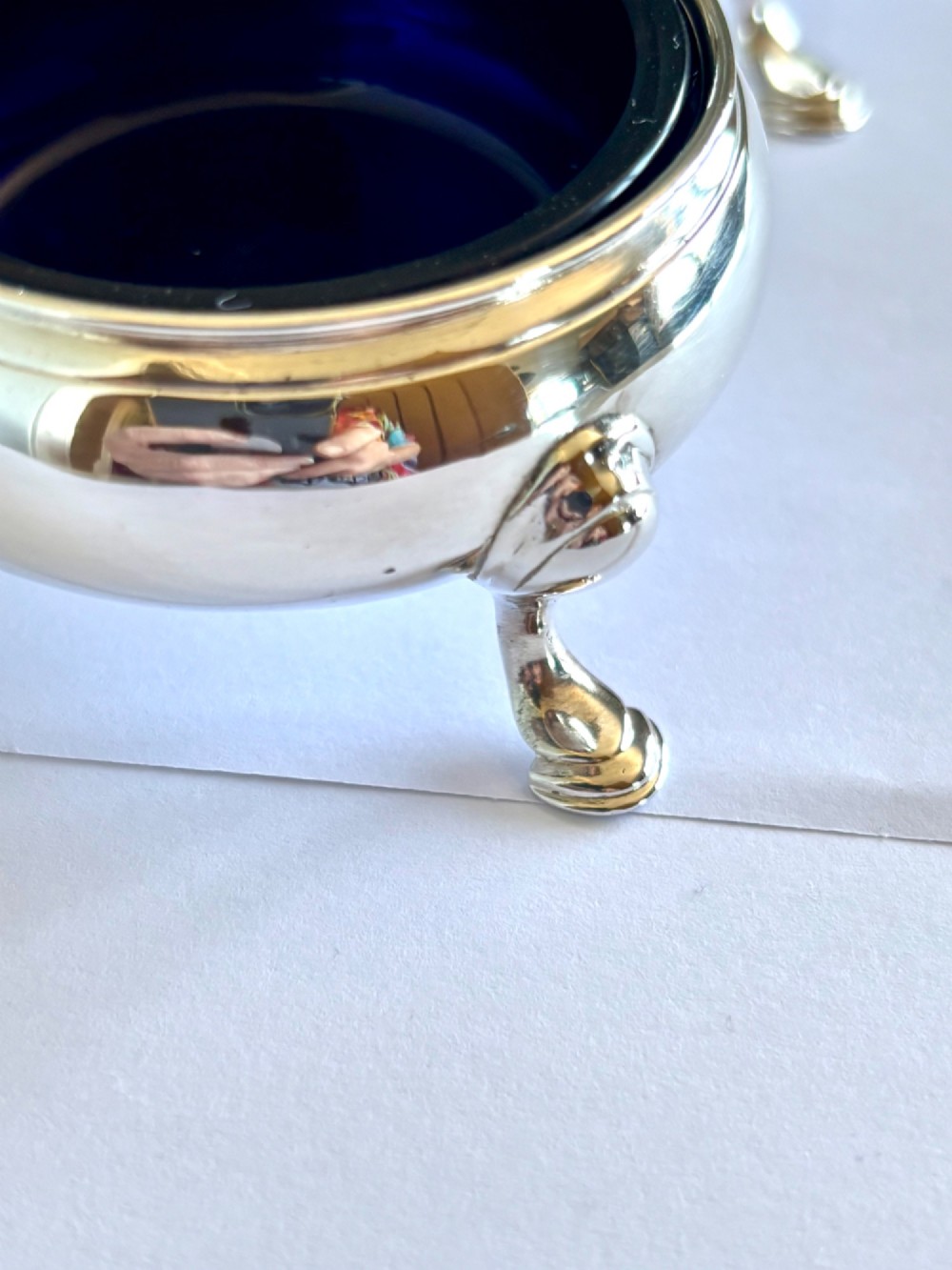 A pair of round 18th-century sterling silver open salt cellars with cobalt blue glass liners, raised on three hoof feet. View X