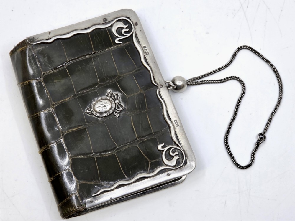 An Art Nouveau dark brown crocodile skin purse featuring hallmarked sterling silver whiplash corner mounts, a central silver cartouche with bow detailing, and a silver chain strap. View II