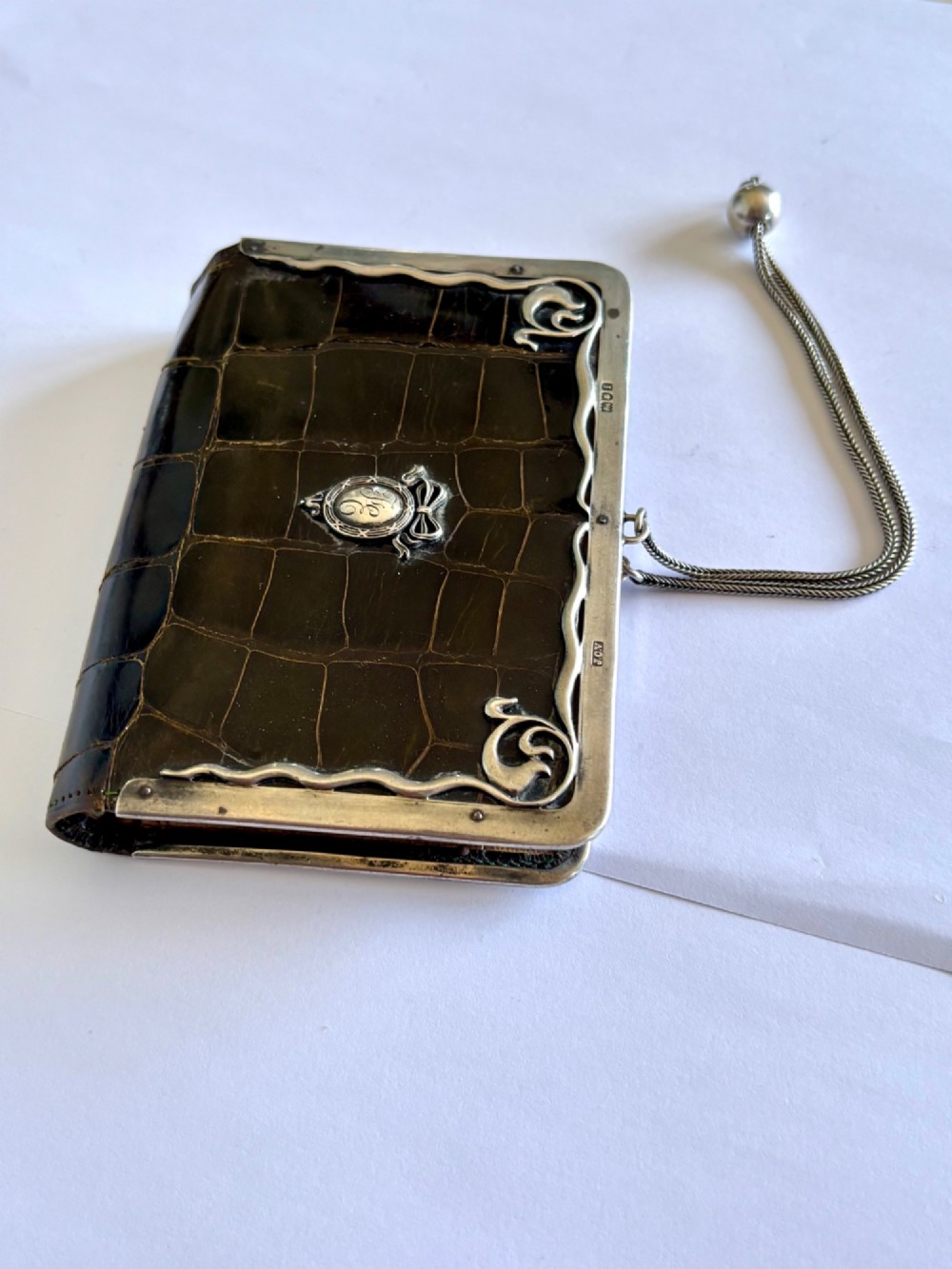An Art Nouveau dark brown crocodile skin purse featuring hallmarked sterling silver whiplash corner mounts, a central silver cartouche with bow detailing, and a silver chain strap. View III