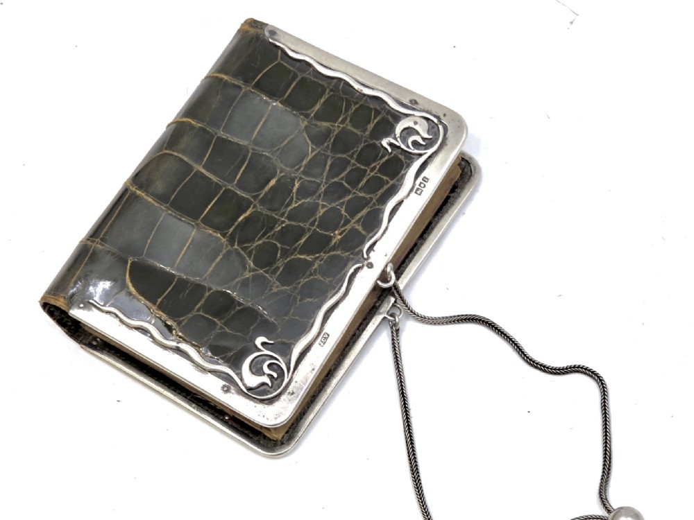 An Art Nouveau dark brown crocodile skin purse featuring hallmarked sterling silver whiplash corner mounts, a central silver cartouche with bow detailing, and a silver chain strap. View IV