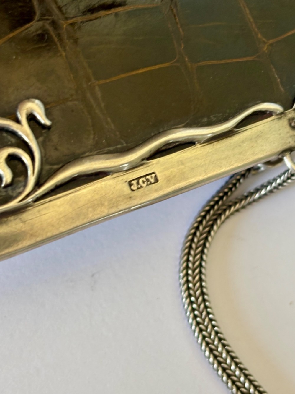 An Art Nouveau dark brown crocodile skin purse featuring hallmarked sterling silver whiplash corner mounts, a central silver cartouche with bow detailing, and a silver chain strap. View VII
