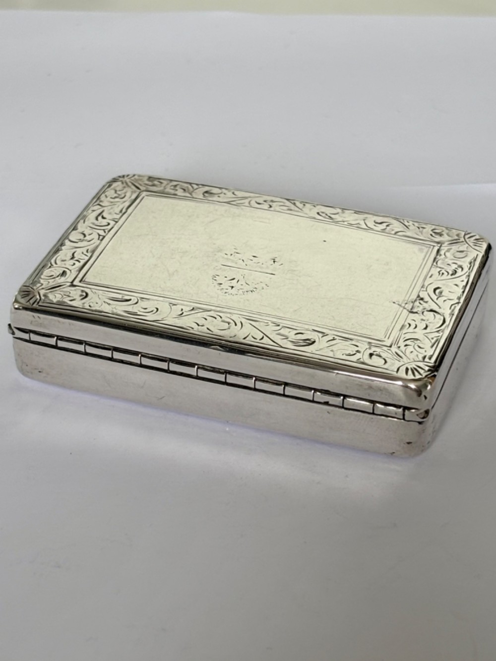 An early Victorian rectangular sterling silver gilt snuff box featuring engraved foliate scroll borders around a central crest on the hinged lid. View II