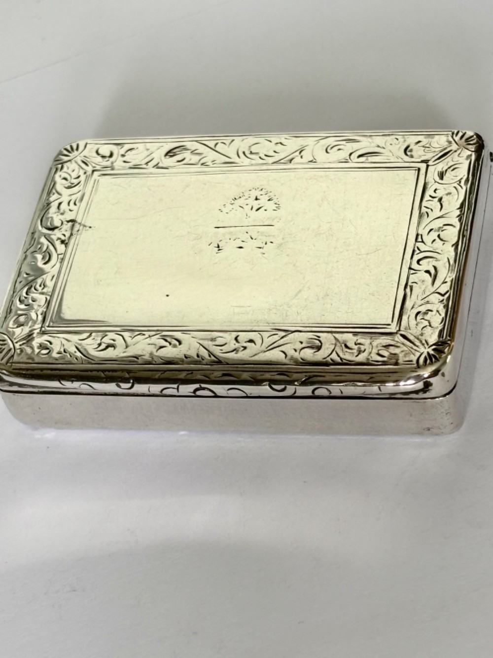 An early Victorian rectangular sterling silver gilt snuff box featuring engraved foliate scroll borders around a central crest on the hinged lid. View III