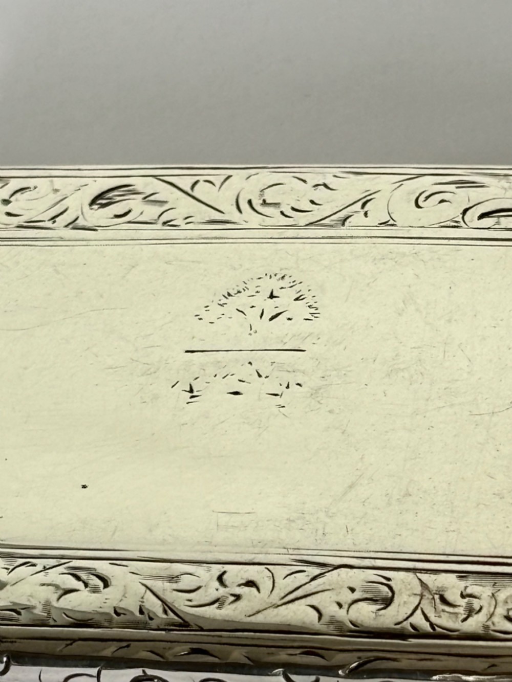 An early Victorian rectangular sterling silver gilt snuff box featuring engraved foliate scroll borders around a central crest on the hinged lid. View IV