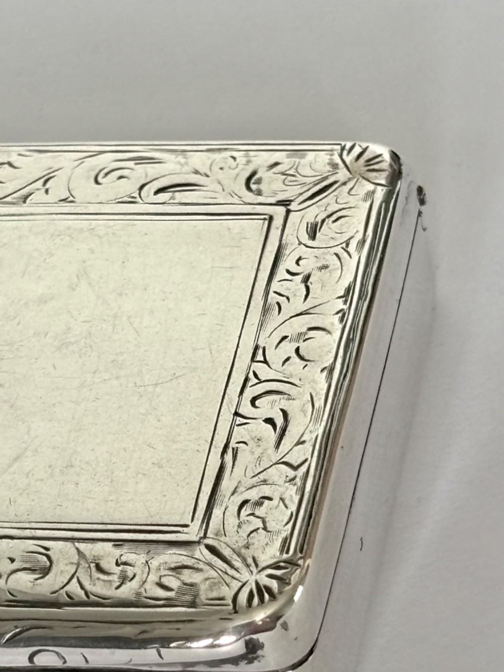 An early Victorian rectangular sterling silver gilt snuff box featuring engraved foliate scroll borders around a central crest on the hinged lid. View V