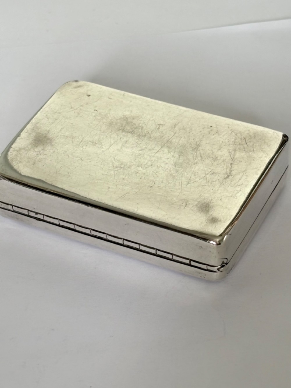 An early Victorian rectangular sterling silver gilt snuff box featuring engraved foliate scroll borders around a central crest on the hinged lid. View VI