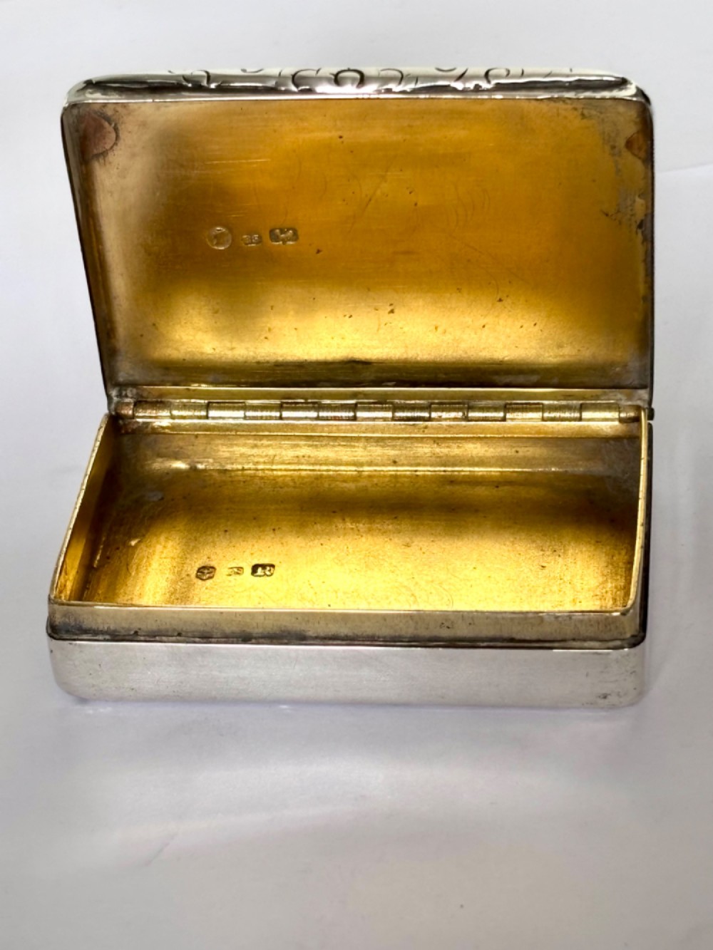 An early Victorian rectangular sterling silver gilt snuff box featuring engraved foliate scroll borders around a central crest on the hinged lid. View IX