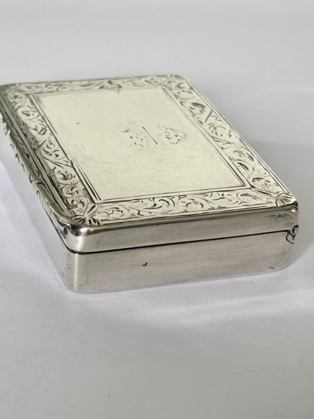 An early Victorian rectangular sterling silver gilt snuff box featuring engraved foliate scroll borders around a central crest on the hinged lid. View XI